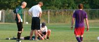 Soccer players and a coach attending to an injured player on the field.